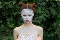 Nice girl cosmetic mask Offended glance green bushes skin care leaves in the background