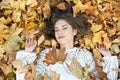 Nice girl covered with autumnal leaves. Young woman laying down on the ground covered by fall foliage in park. Beautiful girl Royalty Free Stock Photo