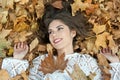 Nice girl covered with autumnal leaves. Young woman laying down on the ground covered by fall foliage in park. Beautiful girl