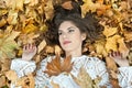 Nice girl covered with autumnal leaves. Young woman laying down on the ground covered by fall foliage in park. Beautiful girl Royalty Free Stock Photo