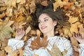 Nice girl covered with autumnal leaves. Young woman laying down on the ground covered by fall foliage in park. Beautiful girl Royalty Free Stock Photo