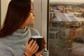 Nice girl drinks coffee and looks out the window at sunset