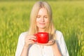 Beautiful young woman drinking tea/coffee outdoors. Green summer field background. Royalty Free Stock Photo