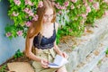 Nice girl in glasses with white hair on a background of a flowering rose bush is reading a book Royalty Free Stock Photo