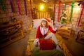 Nice girl in a red dress and hat of Santa with big red gift box in room decorated for Christmas. Woman in beautirul studio during Royalty Free Stock Photo