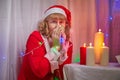 Nice girl in red dress and hat of Santa in room with candles before Christmas. Woman in beautirul studio during photo Royalty Free Stock Photo