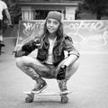 Nice girl, teenager, in a baseball cap sits on a skateboard in a skate park. Black and white photo. Youth Lifestyle. Sport