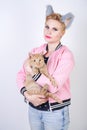 Nice kind woman with a short haircut and fur ears in sports clothes and jeans is holding her beloved pet on a white background in