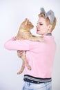 Nice kind woman with a short haircut and fur ears in sports clothes and jeans is holding her beloved pet on a white background in