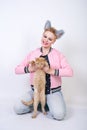 Nice kind woman with a short haircut and fur ears in sports clothes and jeans is holding her beloved pet on a white background in