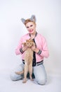 Nice kind woman with a short haircut and fur ears in sports clothes and jeans is holding her beloved pet on a white background in