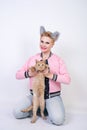 Nice kind woman with a short haircut and fur ears in sports clothes and jeans is holding her beloved pet on a white background in Royalty Free Stock Photo