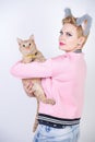 Nice kind woman with a short haircut and fur ears in sports clothes and jeans is holding her beloved pet on a white background in