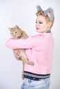 Nice kind woman with a short haircut and fur ears in sports clothes and jeans is holding her beloved pet on a white background in