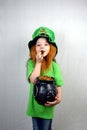 Nice littel girl with decorative red beard in green dress and leprechaun\'s hat, kissing golden coin with four-petal shamrock