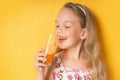 Nice little girl with blond hair enjoying carrot juice with great pleasure showing beautiful smile. Close up shot