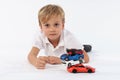 Nice looking very young boy lying with a pile of car toys and having a sincere neutral and proud look in his face