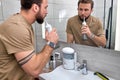 Nice man cleans teeth using electric oral irrigator with jet of water, looking at mirror. Royalty Free Stock Photo