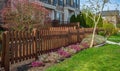 Nice new wooden fence around house. Wooden brown fence with green lawn and nicely landscaped front yard in spring
