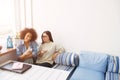 Nice picture of students sitting close to each other on sofa. THey are holding phones in their hands. Afro american girl