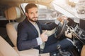 Nice picture of young businessman sitting in luxury car and holding big thumb up. He hold one hand on steering wheel Royalty Free Stock Photo