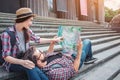 Nice picture of young tourists on stairs. She sits there and points on map. He holds map and lies on woman`s knees.