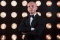 Nice portrait of professional illusionist. Magician in black suit standing in the room with special lighting at