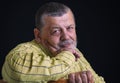 Portrait of a smiling senior man in yellow shirt leant elbow on a back of chair against black