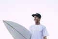 Nice portrait of young teenager with white surf board and t-shirt smiling and looking at his side - white clear sky background, Royalty Free Stock Photo