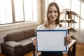 Nice positive businesswoman stand in room and pose on camera. She hold plastic tablet in piece of paper and show it.