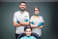 Nice positive male and female dentist with girl in dental chair. They look straight and smile. Adults hold hands crossed