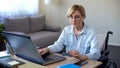 Nice senior woman in wheelchair typing card number on laptop, paying bills Royalty Free Stock Photo