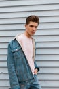 Nice sexy young man with hairstyle with stylish blue denim jacket in pink fashionable sweatshirt near white wall in city. Fashion Royalty Free Stock Photo