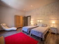 Nice shot of spacious room with two single beds, light walls, wooden floor, red carpet and armchair