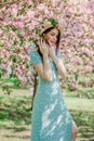 Nice slim young girl in blue dress and straw hat stay in blooming garden