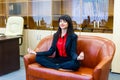 Nice smiling businesswoman sitting on sofa in the lotus positi