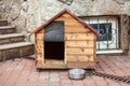 Nice solid wooden doghouse without a dog settled close to the house, with an empty bowl