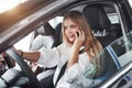 Nice sunbeam above the roof. Beautiful blonde girl sitting in the new car with modern black interior