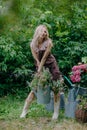 Beautiful girl with long blonde hair holds a watering can with flowers in a blooming garden Royalty Free Stock Photo