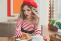 Nice woman in red beret sitting in cafe, drinking coffee and eating french croissant Royalty Free Stock Photo