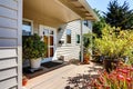 Nice wooden floor porch with flowers and bushes around. Front white entry door. Royalty Free Stock Photo