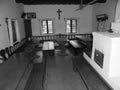 Retro image - Nice wooden polished tables with chairs and benches inside of historic house with white walls and oven with metal do