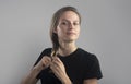 Nice young beautiful caucasian woman braids her hair looking at camera over grey studio background