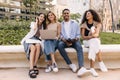 Nice young caucasian, african classmates working in team behind laptop sitting outdoors. Royalty Free Stock Photo