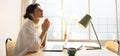 Nice young caucasian girl is praying with palms together and closing eyes indoors by window. Royalty Free Stock Photo