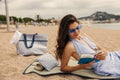 Nice young caucasian woman in sunglasses relaxing and reading book on beach. Royalty Free Stock Photo