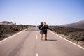 Nice young couple viewed from rear walking together hugging on a long way road in the middle of the lava desert on an asphalt road