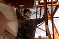 Nice young hipster man in a black knitted hat in a stylish military shirt in trendy sunglasses poses near a vintage iron staircase Royalty Free Stock Photo