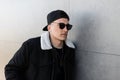 Nice young men hipster in a stylish black jacket in a fashionable black cap in dark trendy sunglasses in a black t-shirt Royalty Free Stock Photo