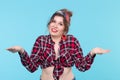 Nice young positive woman in plaid shirt posing over blue background with arms spread to the side. Concept of choice and